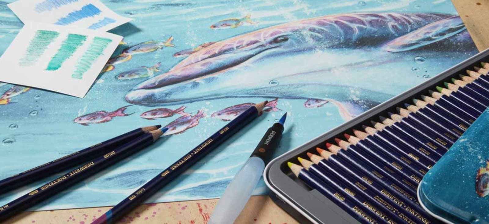 Derwent Inktense pencils lying next to dolphin drawing and waterbrush