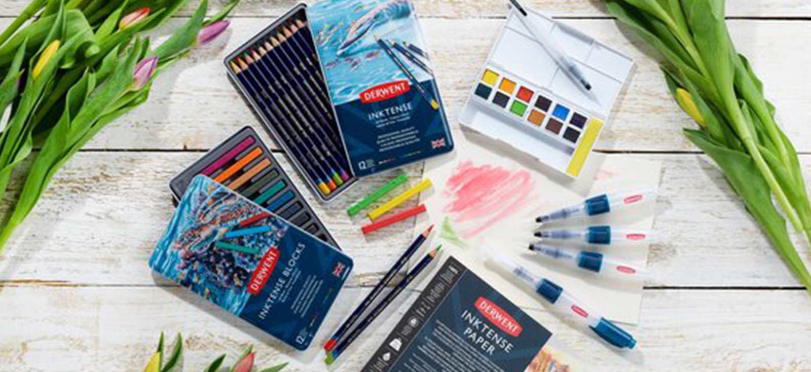 Table spread of Derwent pencils, paint pans and water brushes